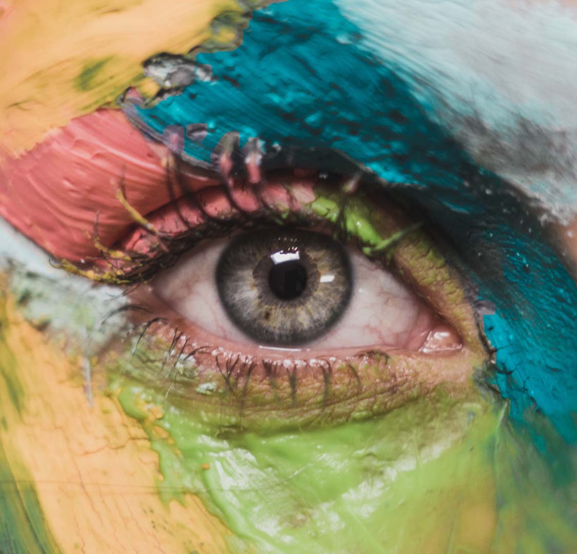 you: a close up of a human eye. The face is painted various vibrant colours suggesting individuality.