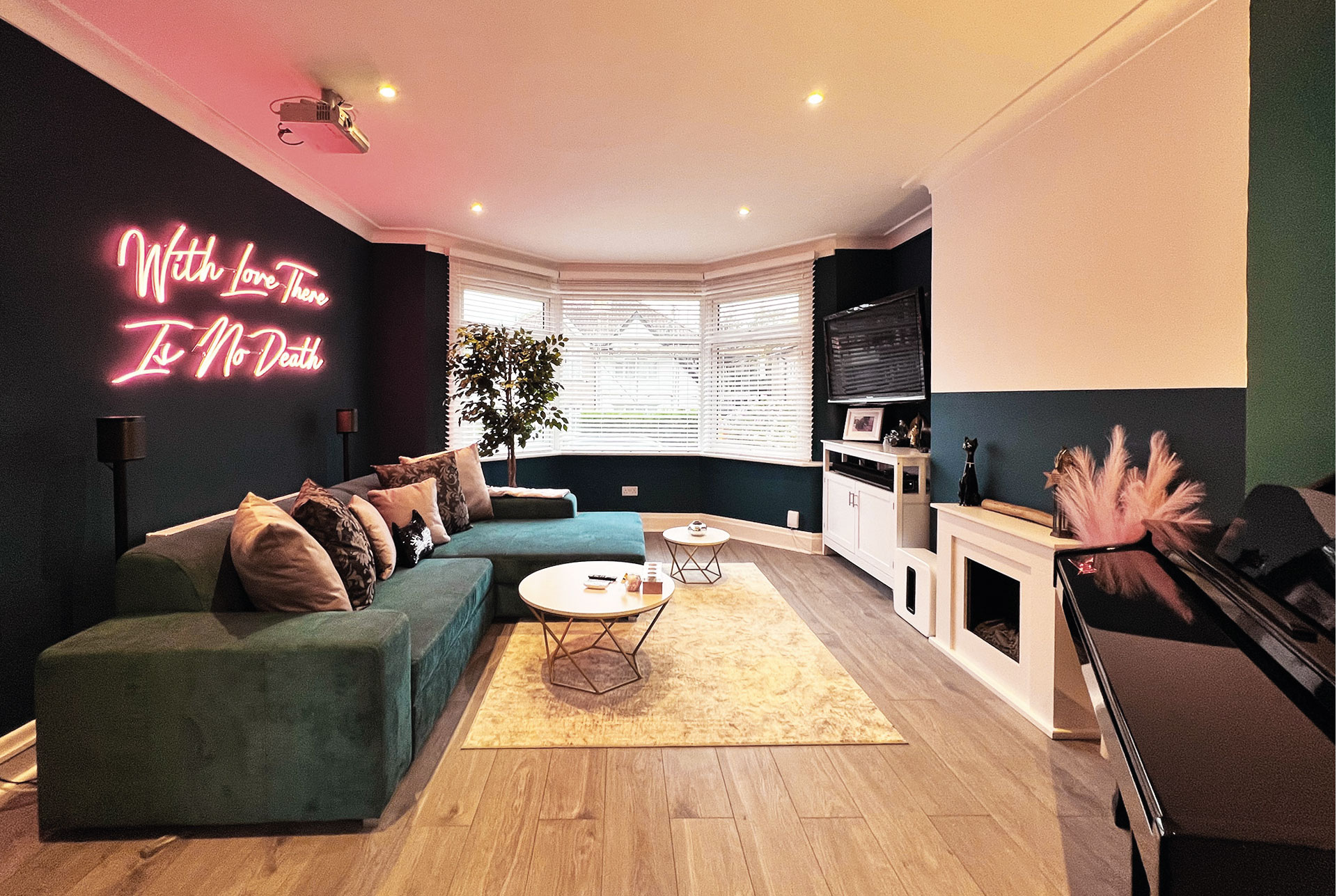 A contemporary lounge with teal and white walls, a modern engineered wood floor with a decorative rug and a luxurious velvet teal L-shaped sofa with a neon light on the wall behind it.