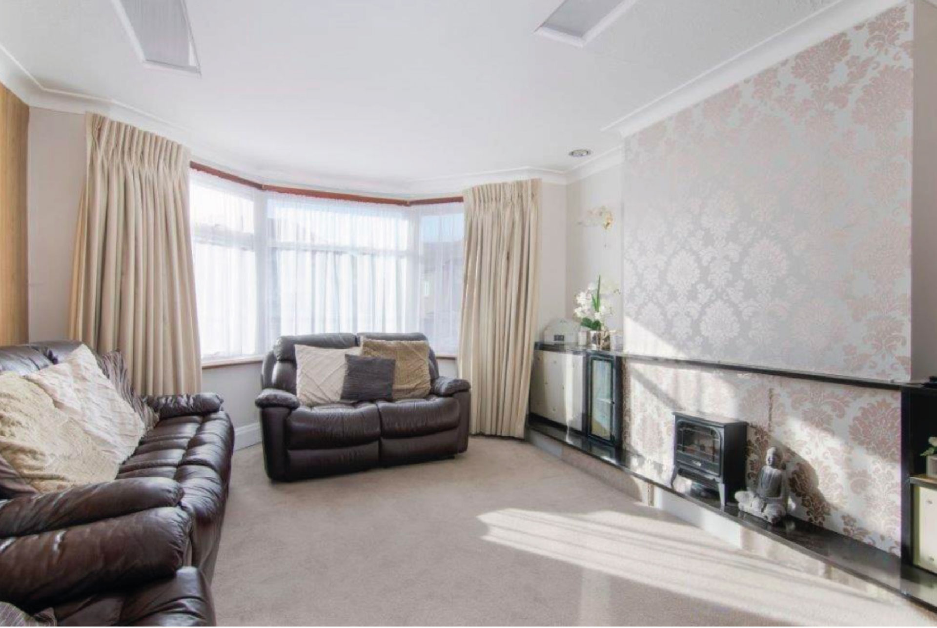 A very plain living room with beige wallpaper and carpets. Furnished with brown leather sofas and built-in cupboards